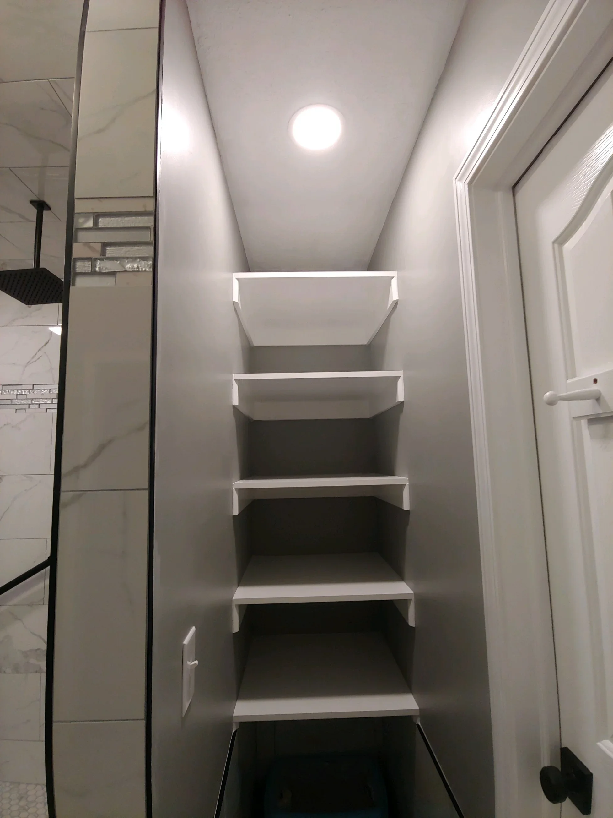 Four white floating shelves with trim in narrow hallway, LED recessed lighting above