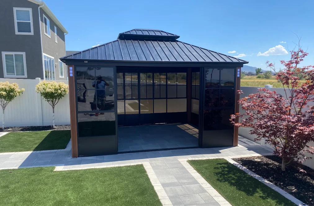 Black metal-roofed gazebo with glass panels and wood posts on concrete pad