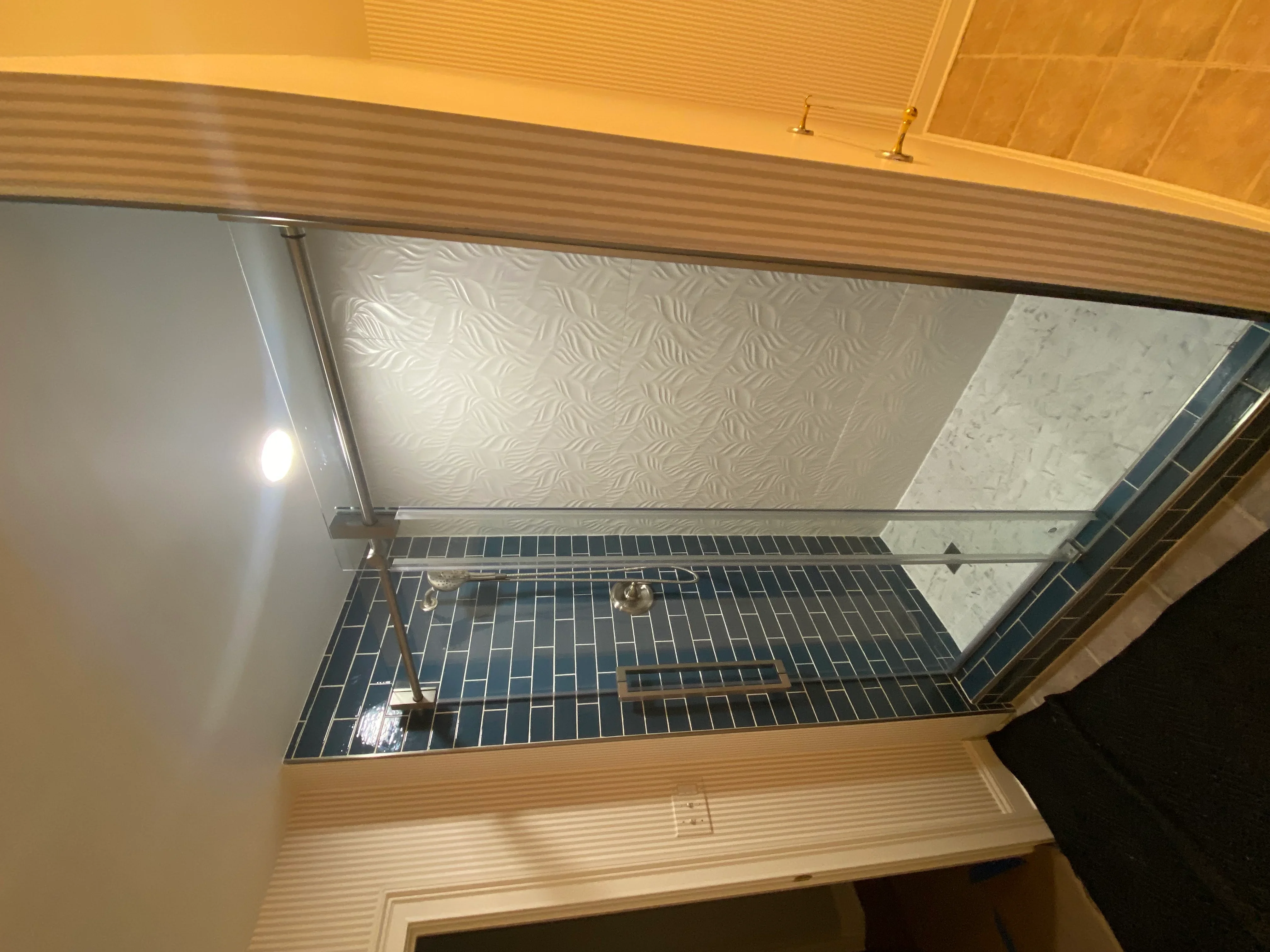 Dark subway tile shower floor with glass enclosure, white textured ceiling tiles, and marble accent wall