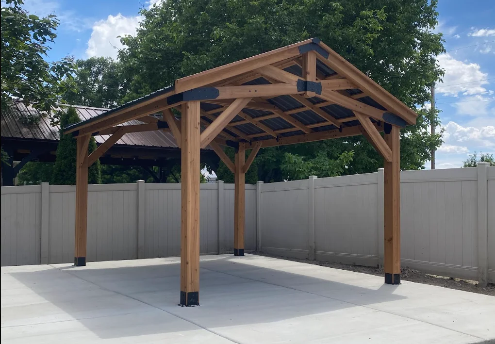 Timber frame carport with gabled roof, wooden beams, steel post bases on concrete pad