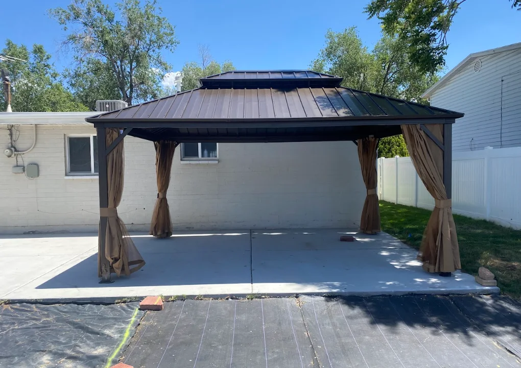 Black metal hardtop gazebo with curtains installed over concrete patio