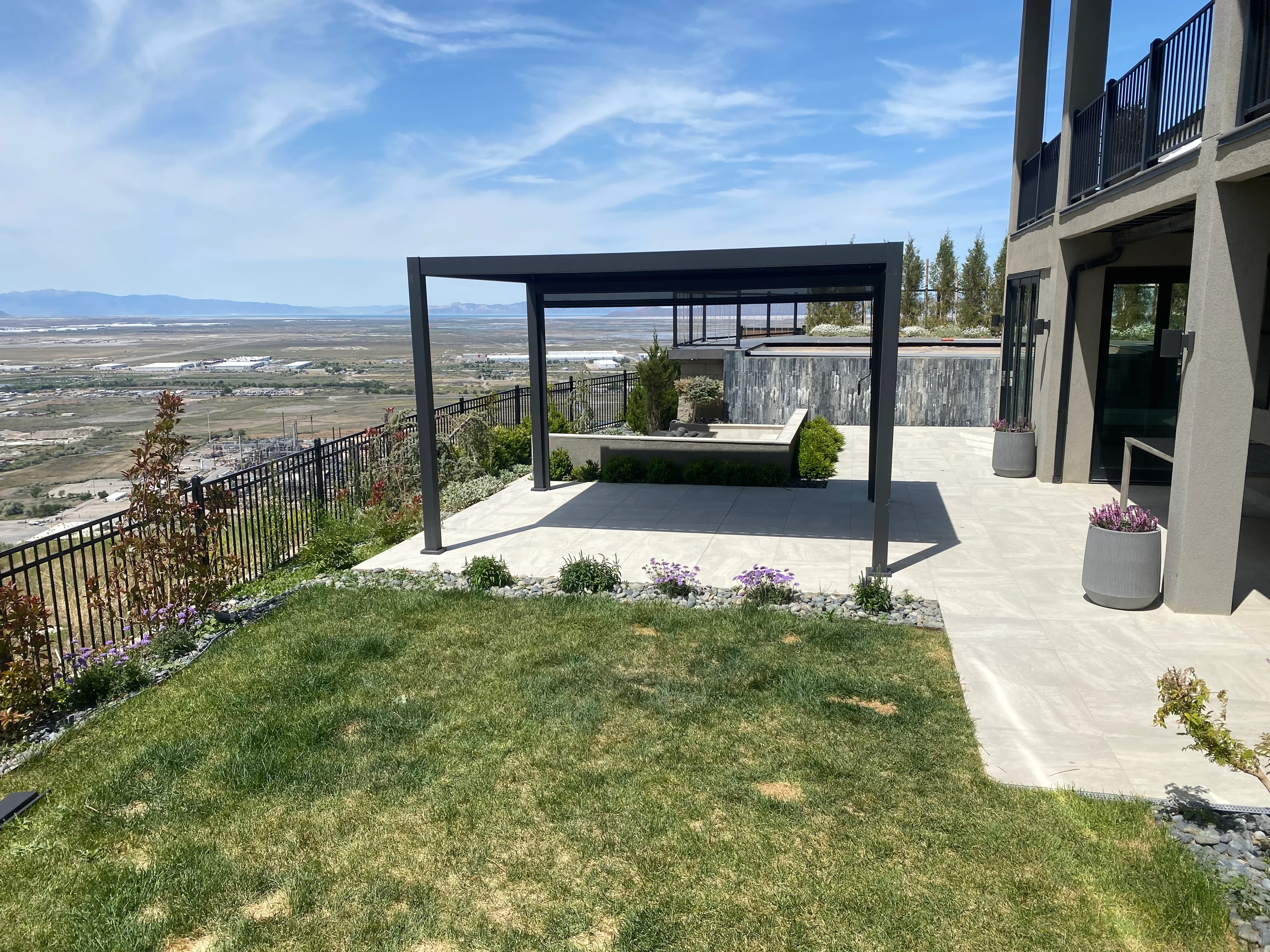 Black steel pergola over concrete patio with hot tub, metal railings, and landscaping