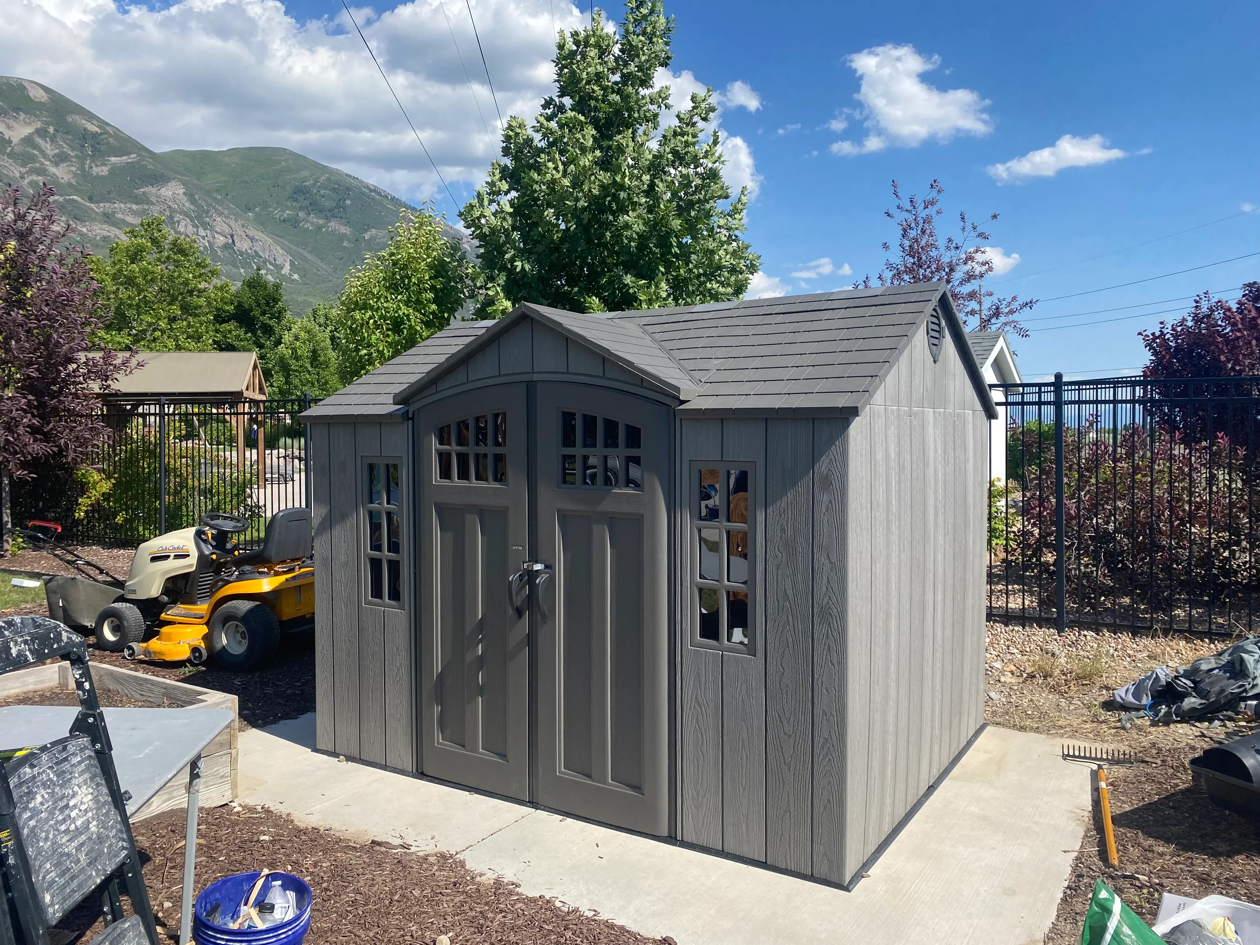 Gray composite storage shed with double doors and windows on concrete foundation