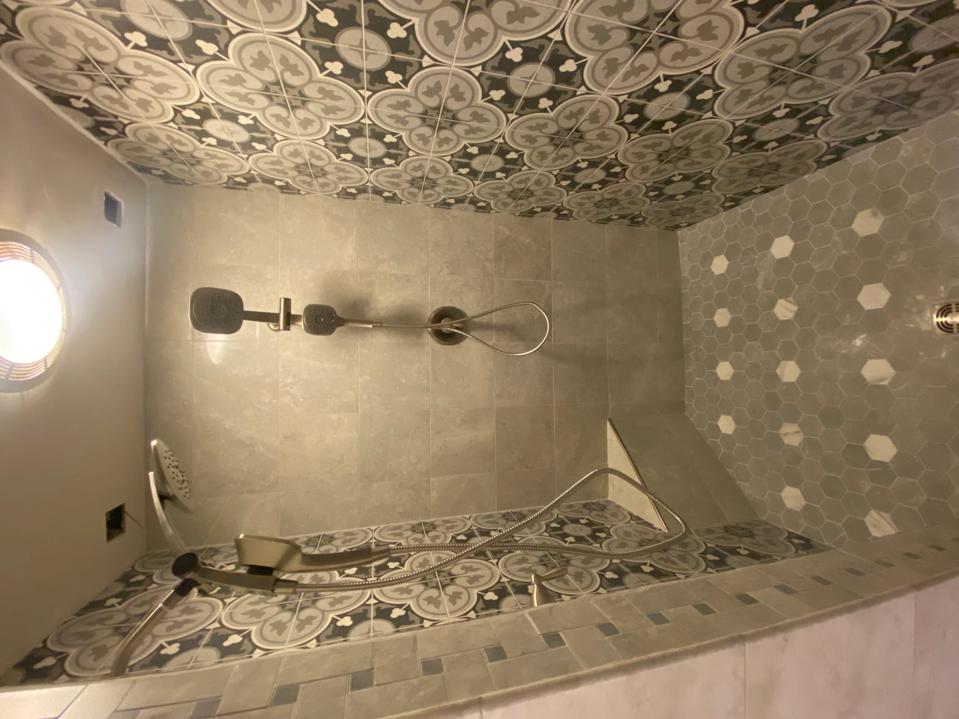 Shower interior with patterned ceiling tile, hexagonal floor mosaic, and glass enclosure