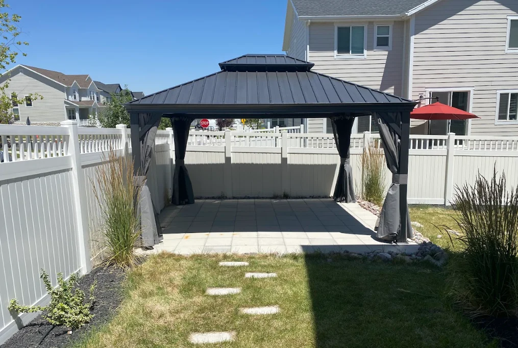 Black metal gazebo with peaked roof and dark curtain panels on concrete pad