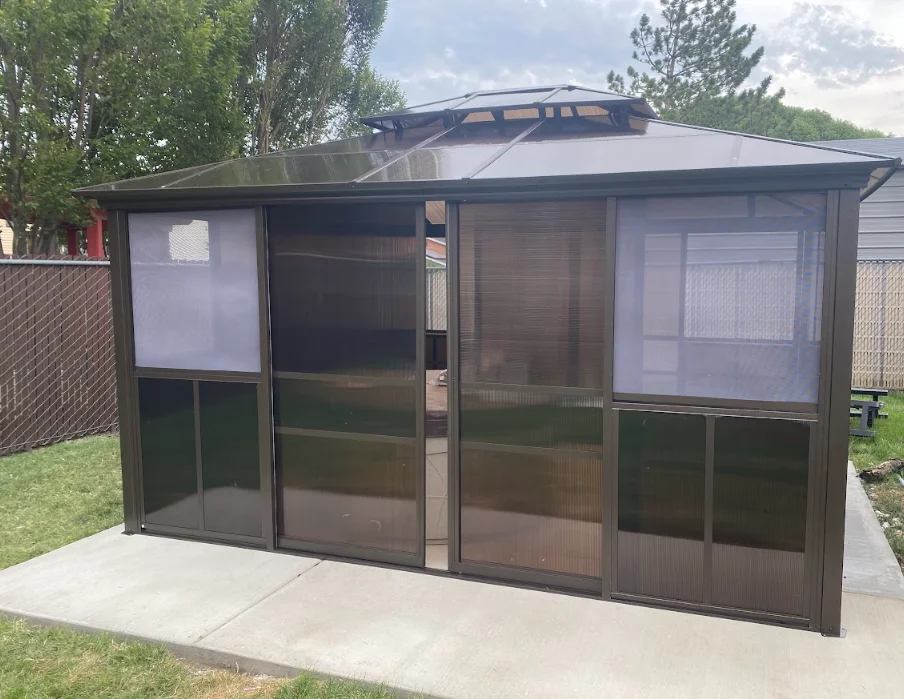 Dark metal frame screened gazebo with bronze polycarbonate panels and sliding doors on concrete pad