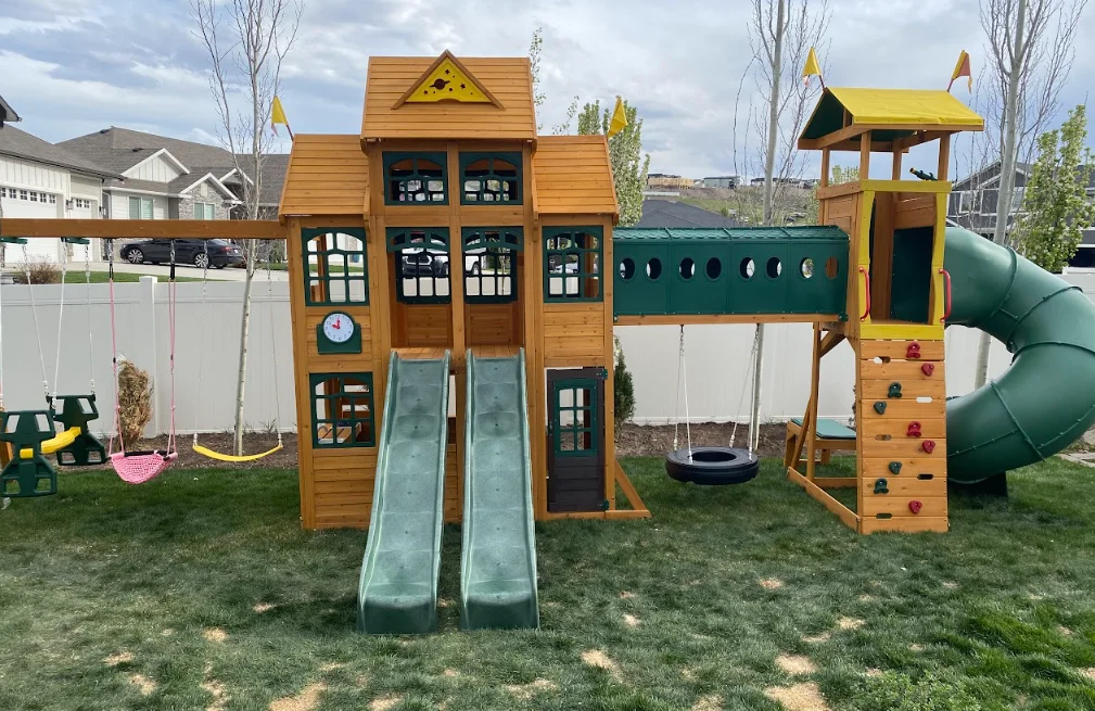 Wooden playset with dual slides, climbing wall, tire swing, and green spiral tube slide