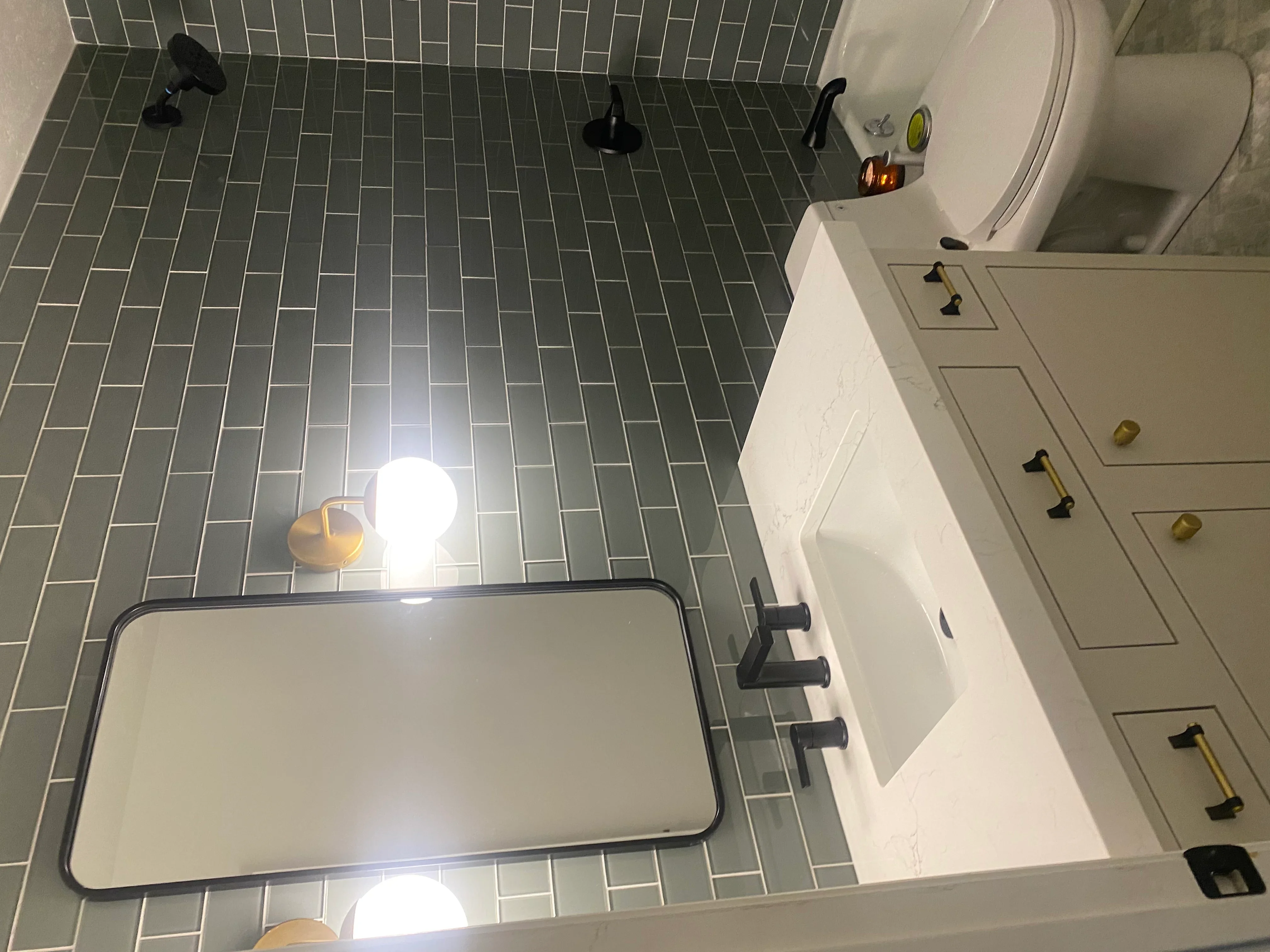 Gray herringbone tile floor with white vanity cabinet, brass hardware, and black fixtures in bathroom
