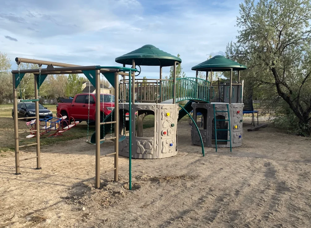 Multi-level playground structures with green canopy roofs, climbing walls, and wooden pergola swing frame on sand base
