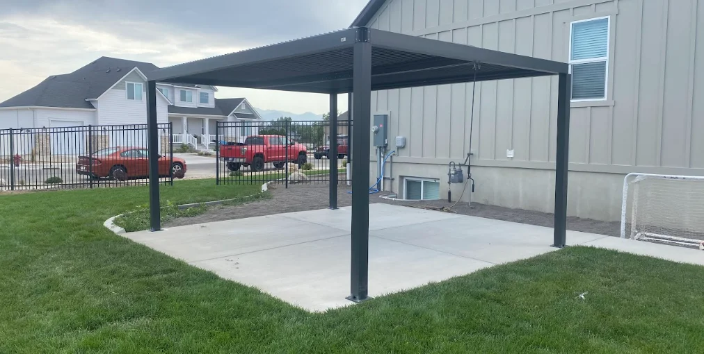 Black aluminum pergola with slatted roof over concrete patio in residential backyard