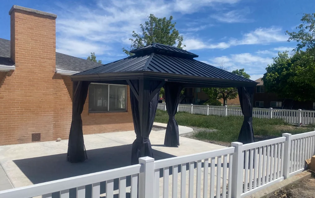 Black metal gazebo with peaked roof and curtain panels on concrete patio with white vinyl railing