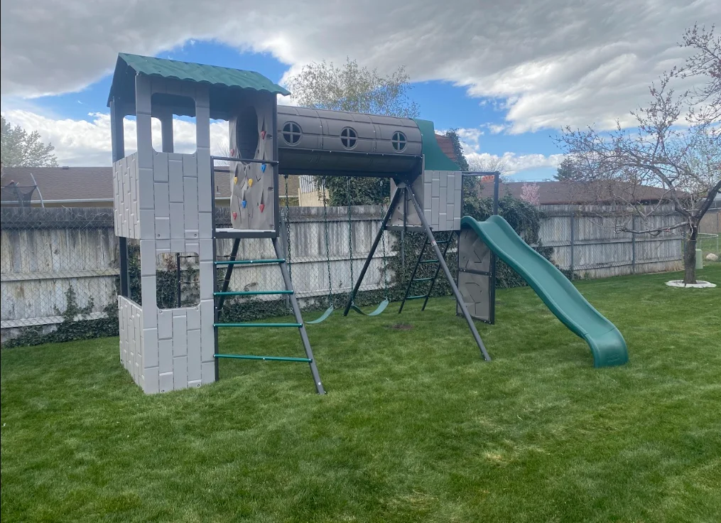 White tower playset with green roof, metal ladder, and slide installed on grass yard