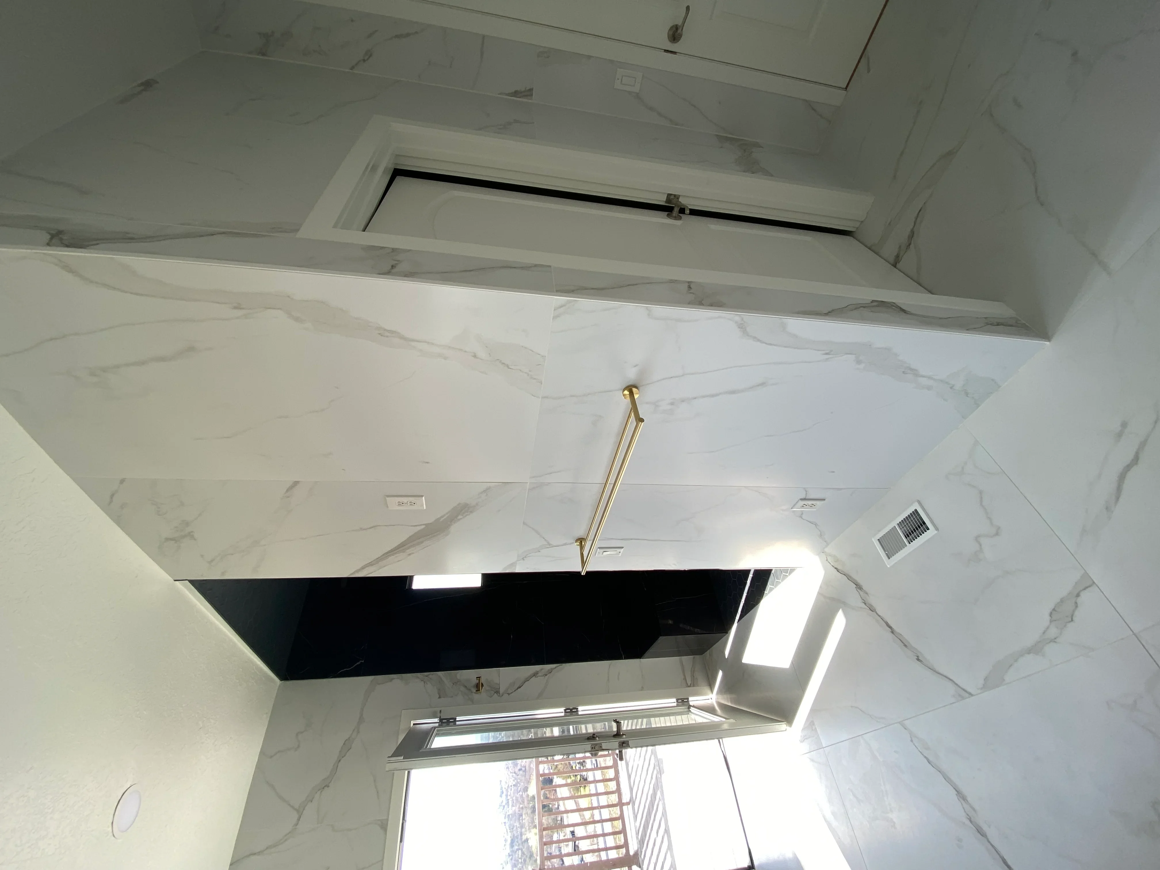 Marble tile ceiling installation with recessed lighting and white soffit framing