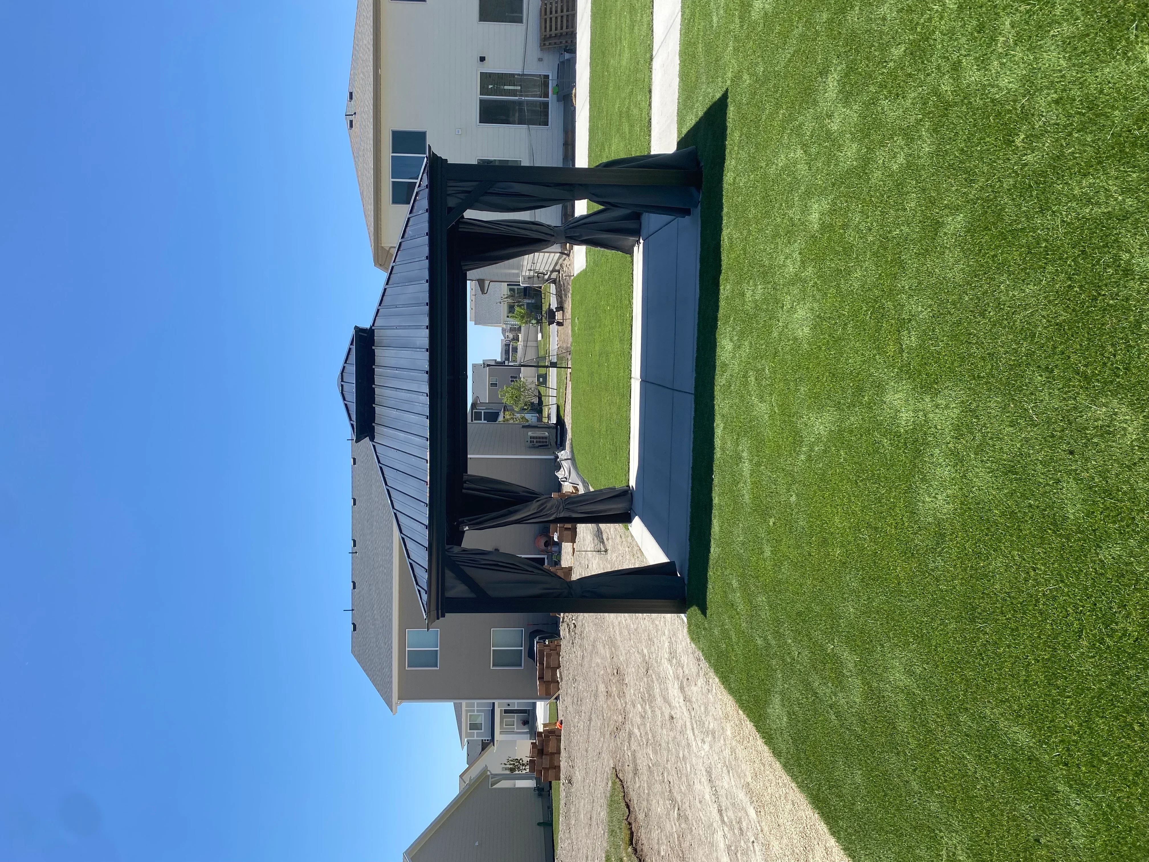 Black pergola with retractable shade panels over concrete patio adjacent to green lawn