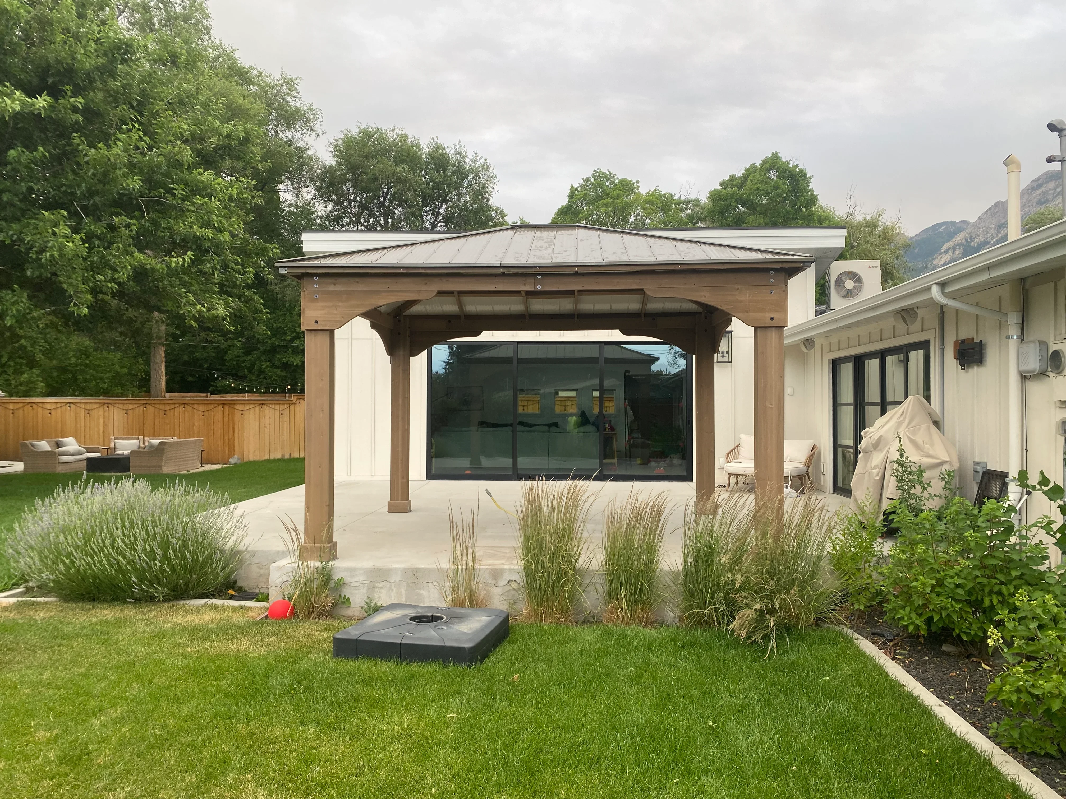 Wooden pergola with retractable shade over concrete patio, ornamental grasses, and mountain backdrop