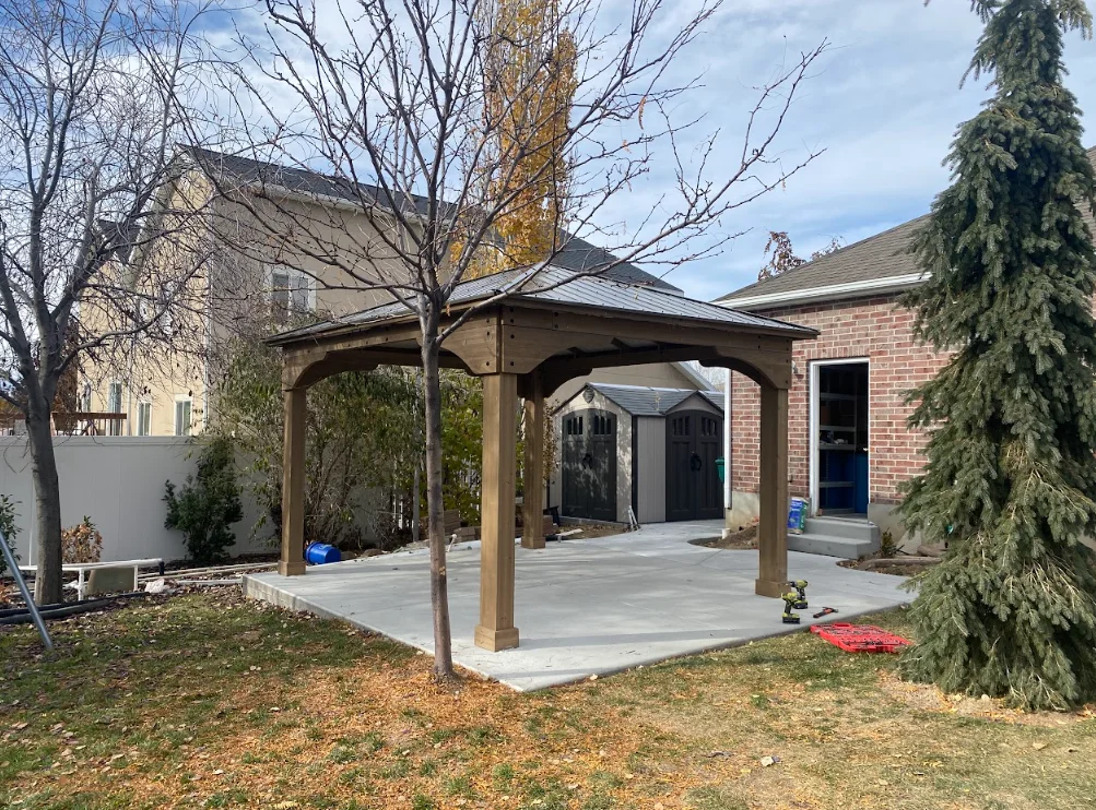 Wooden pergola with arched beams over concrete patio beside brick home