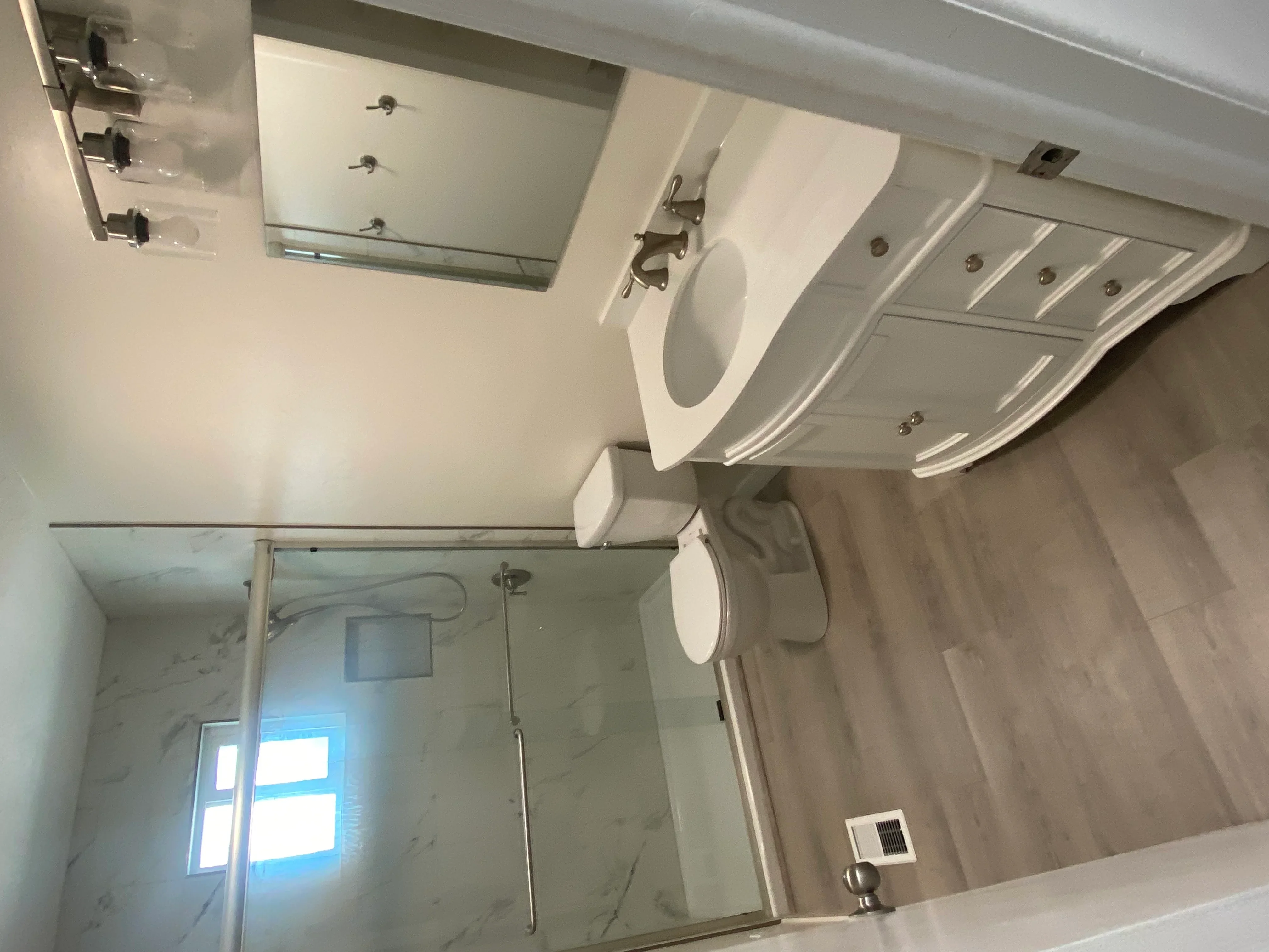 Renovated bathroom with white pedestal sink, toilet, recessed lighting, and marble tile shower surround
