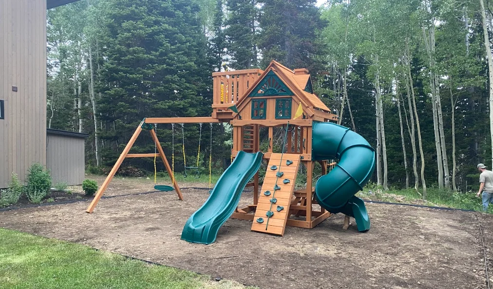 Wooden playset with tower, dual slides, climbing wall, and swings installed in backyard