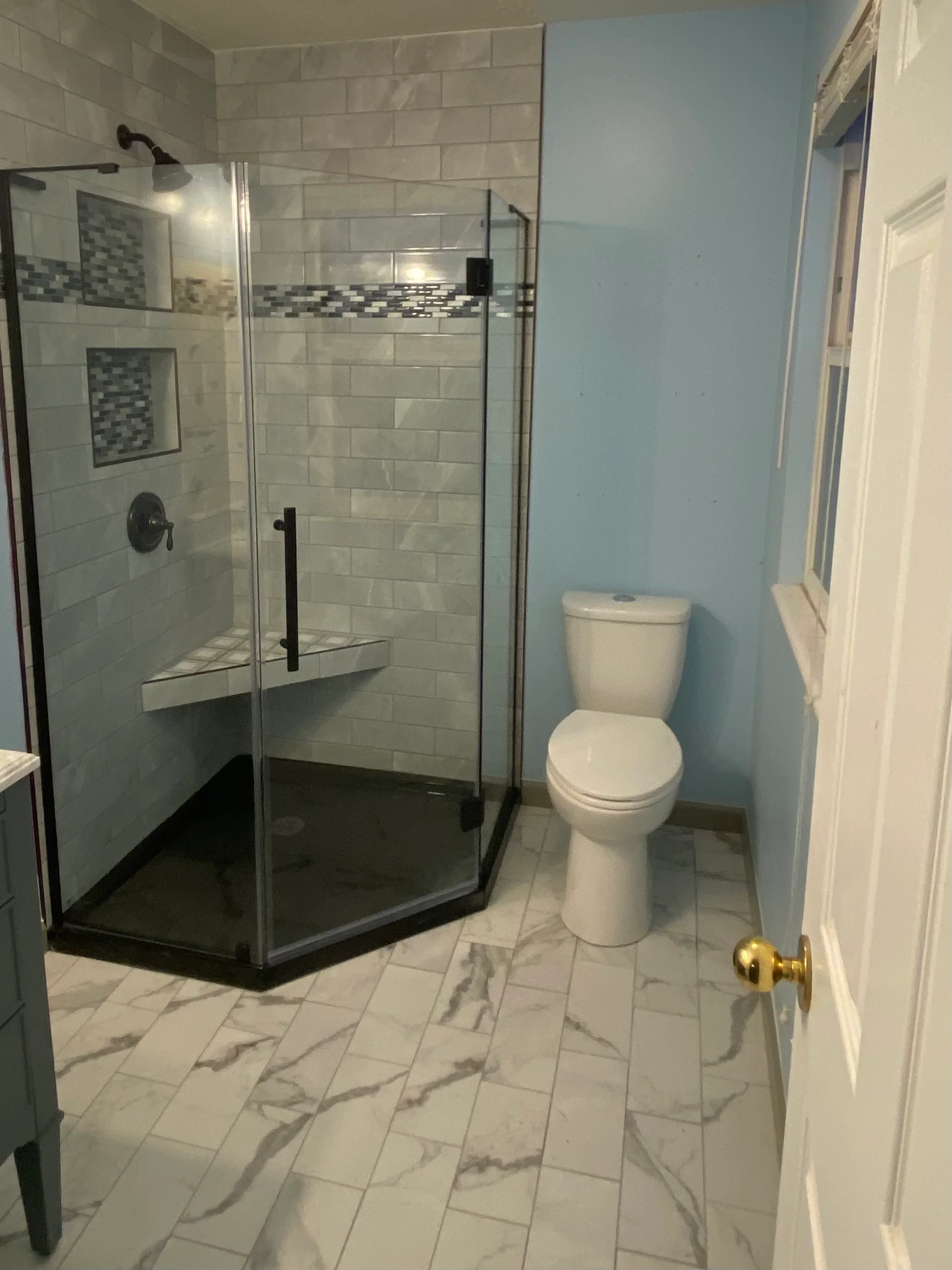 Frameless glass shower with subway tile, mosaic accent, marble-look floor tile, and white toilet