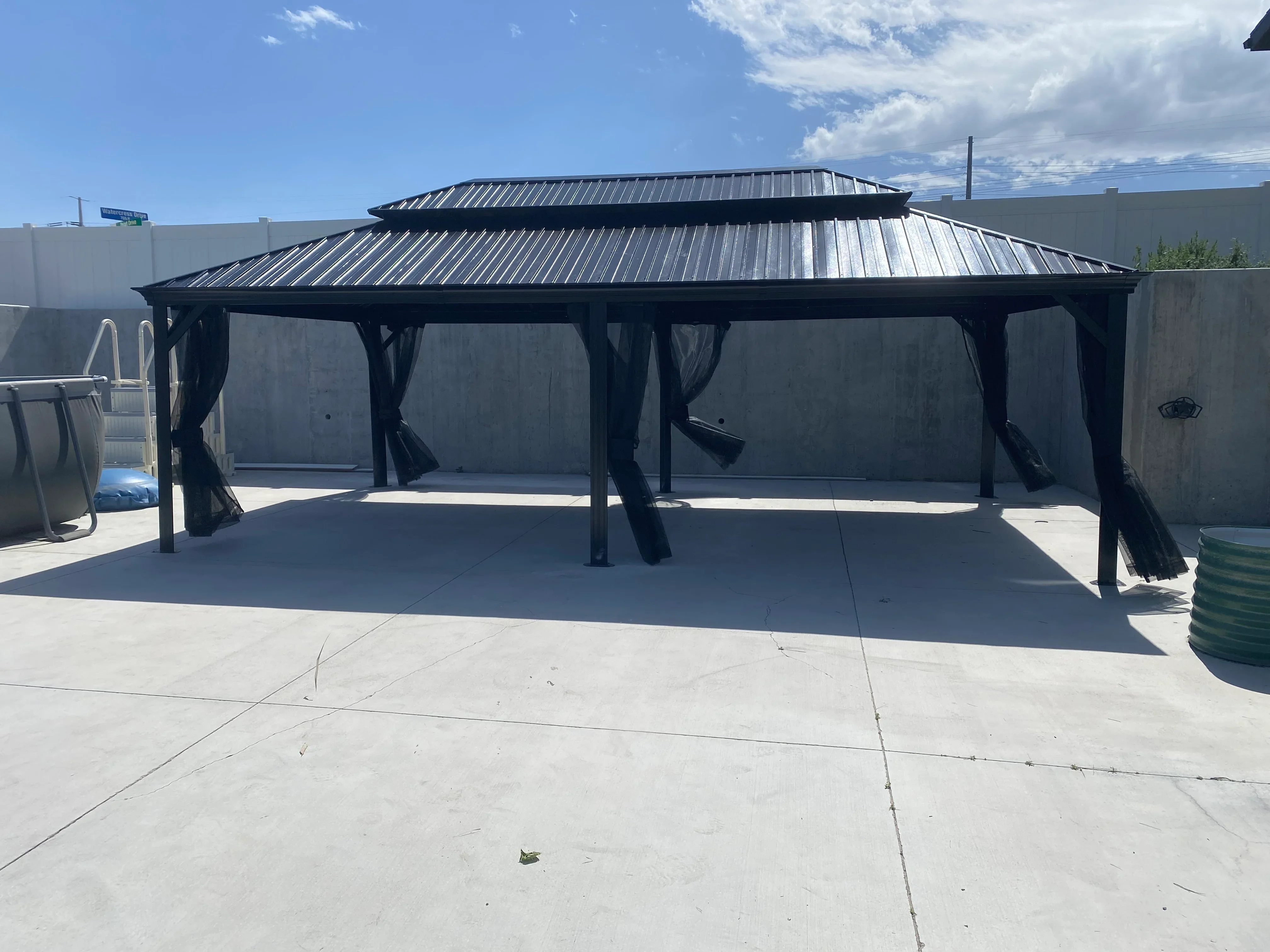 Black metal gazebo with standing seam roof and steel frame on concrete patio