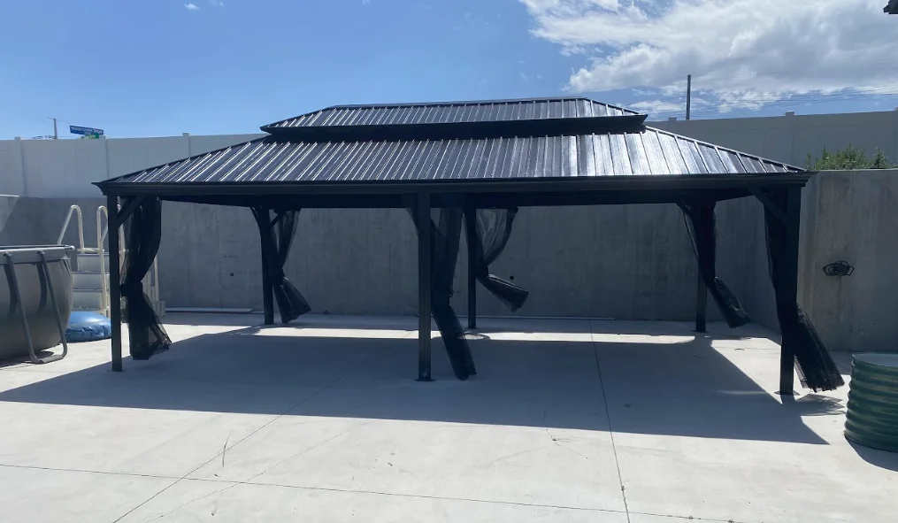 Black metal gazebo with peaked metal roof and fabric curtains on concrete patio