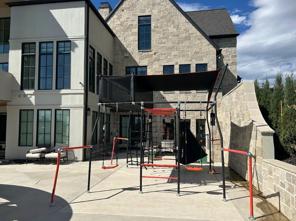 Installed trampoline with black safety enclosure and shade canopy on concrete patio