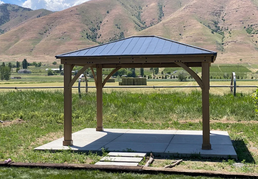 Timber frame gazebo with metal roof on concrete pad in rural setting