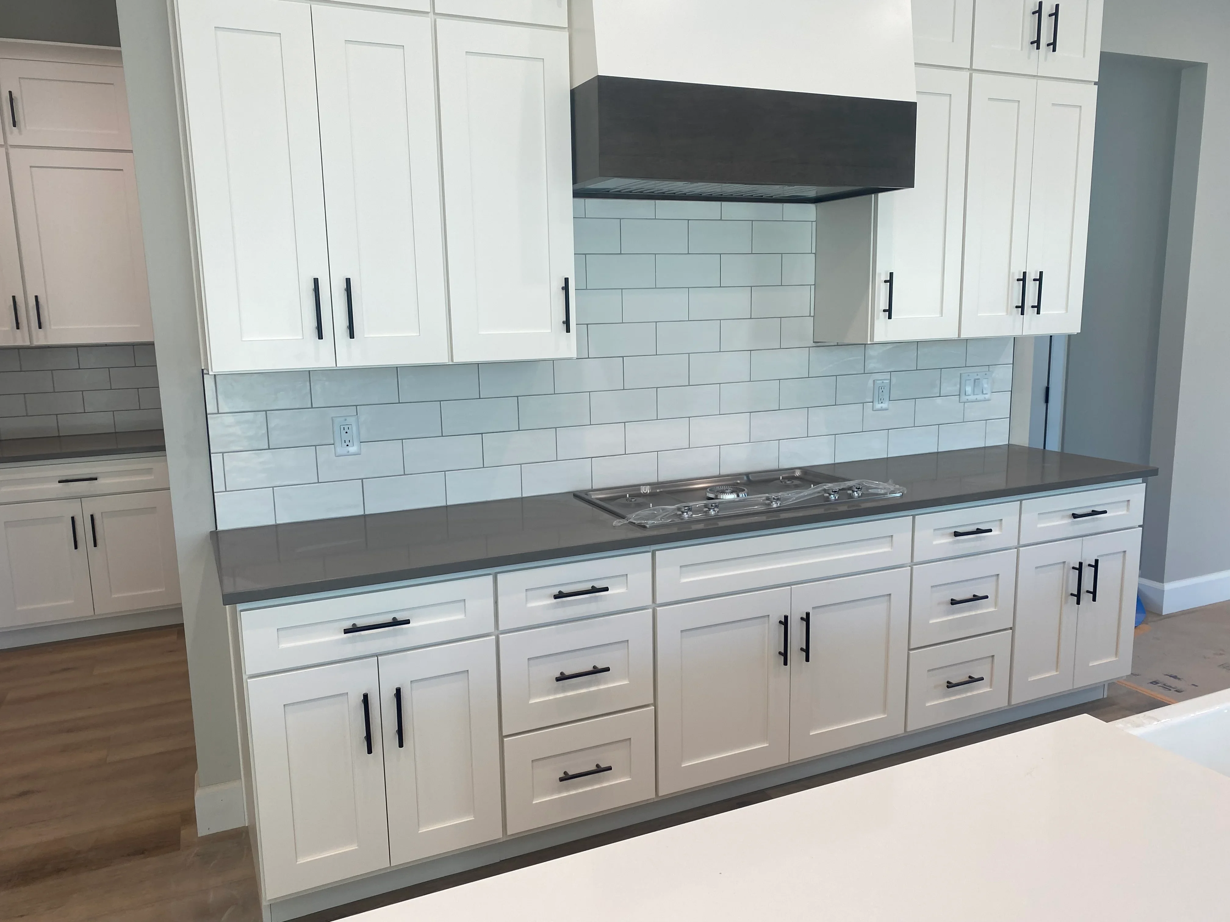White kitchen cabinets with light blue subway tile backsplash and dark gray countertops