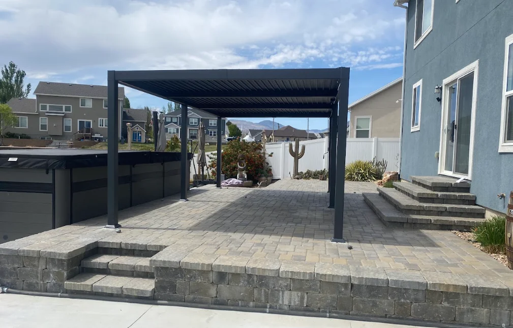 Black pergola over gray paver patio with stone planter wall and desert landscaping
