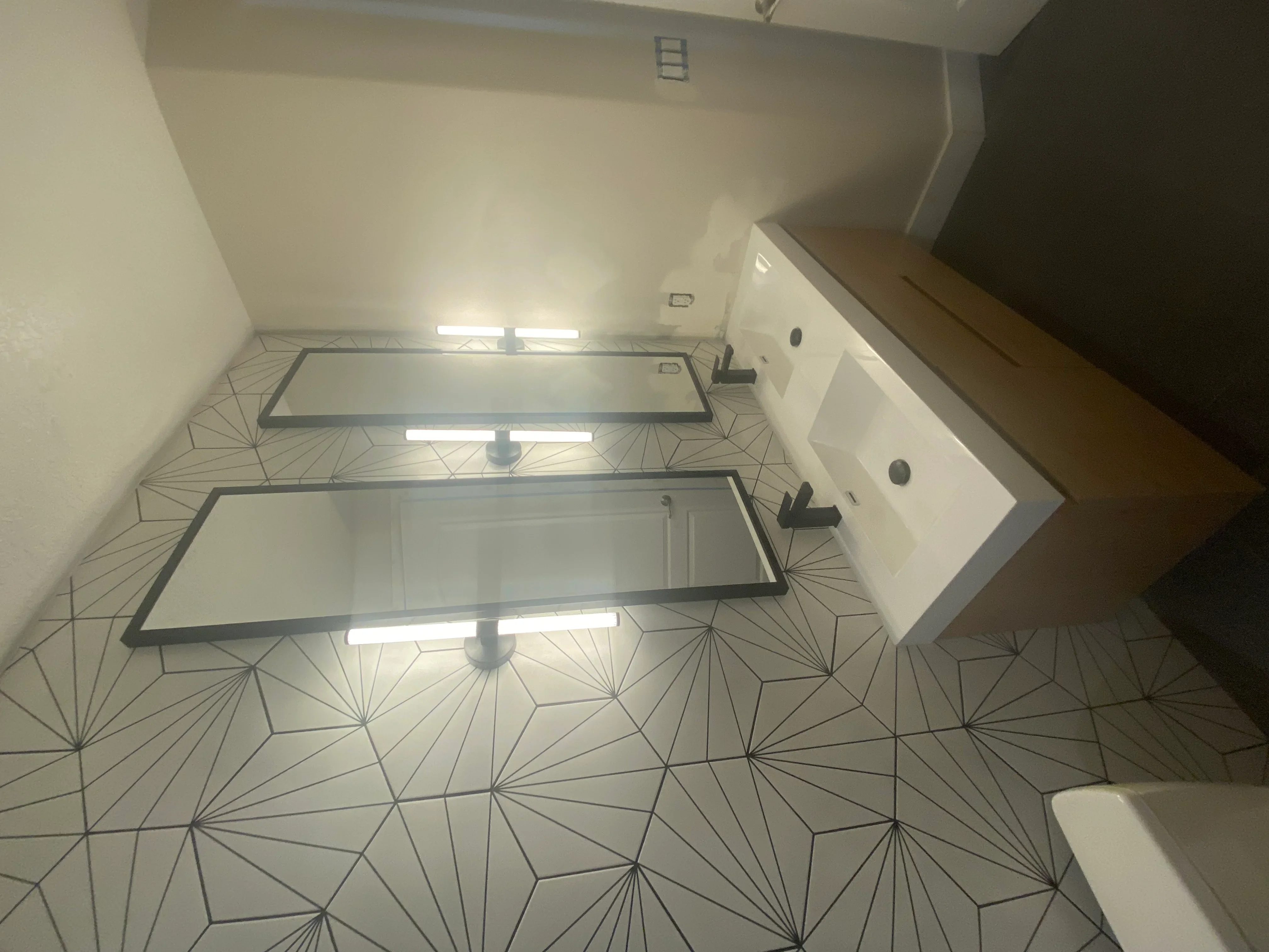 Bathroom with geometric hexagonal floor tile, dual white vanity, recessed lighting, and black fixtures