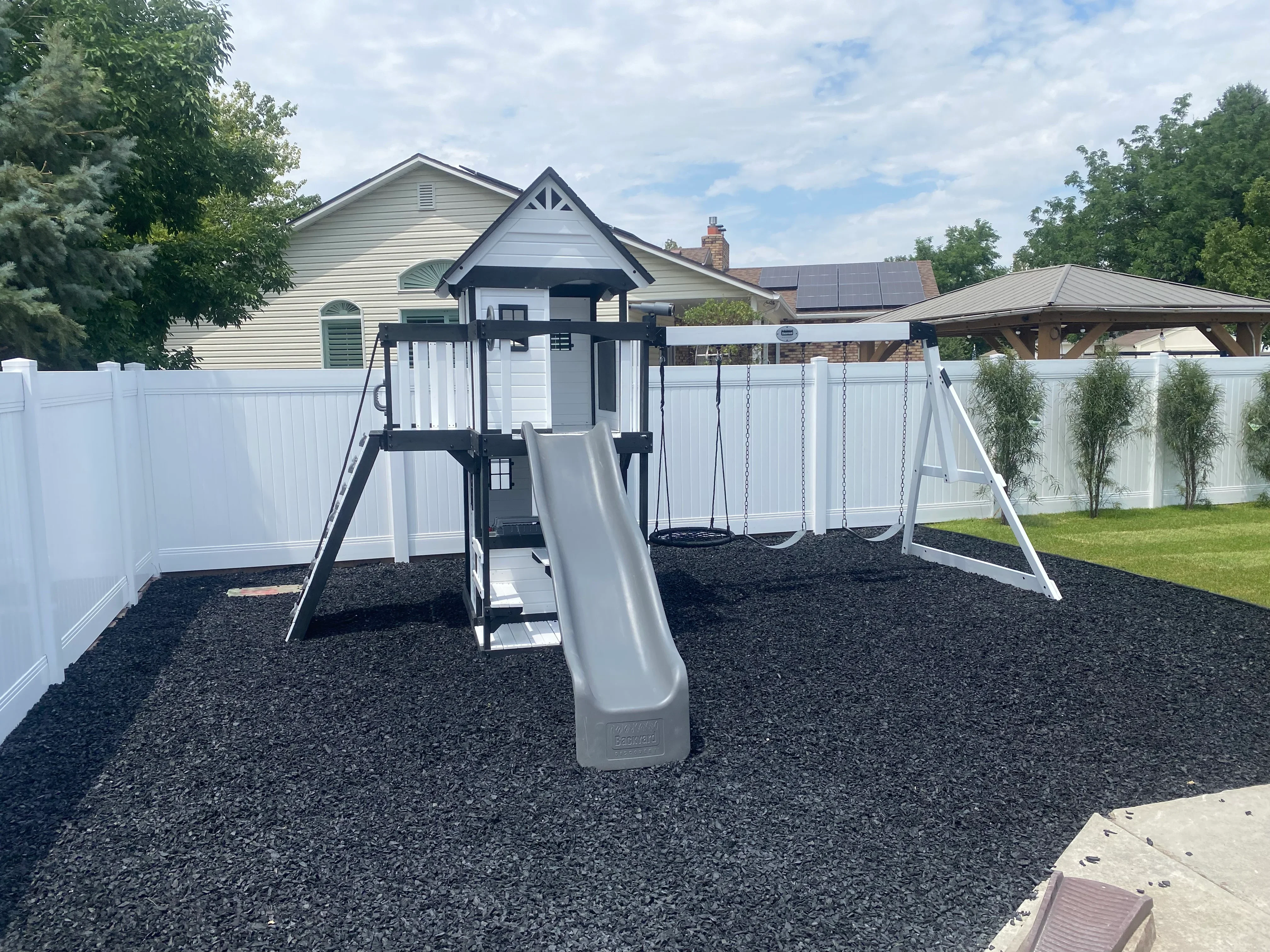 Playground structure with slide and swings, white vinyl fence, black rubber mulch surface