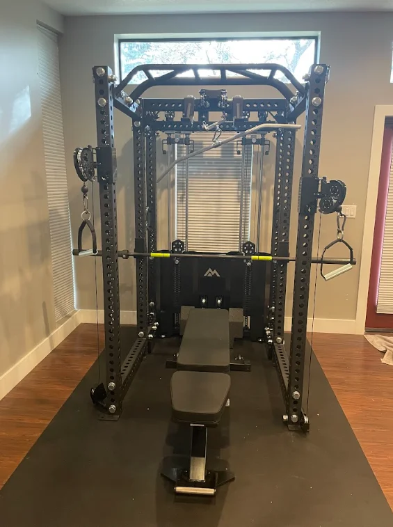 Black steel Smith machine with cable attachments, bench, and rubber mat flooring in home gym