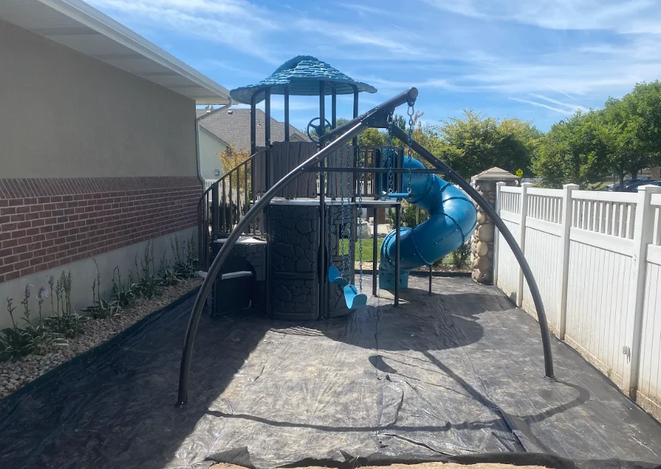 Multi-level playset with blue spiral slide, tower, railings, and rubber safety surface installation