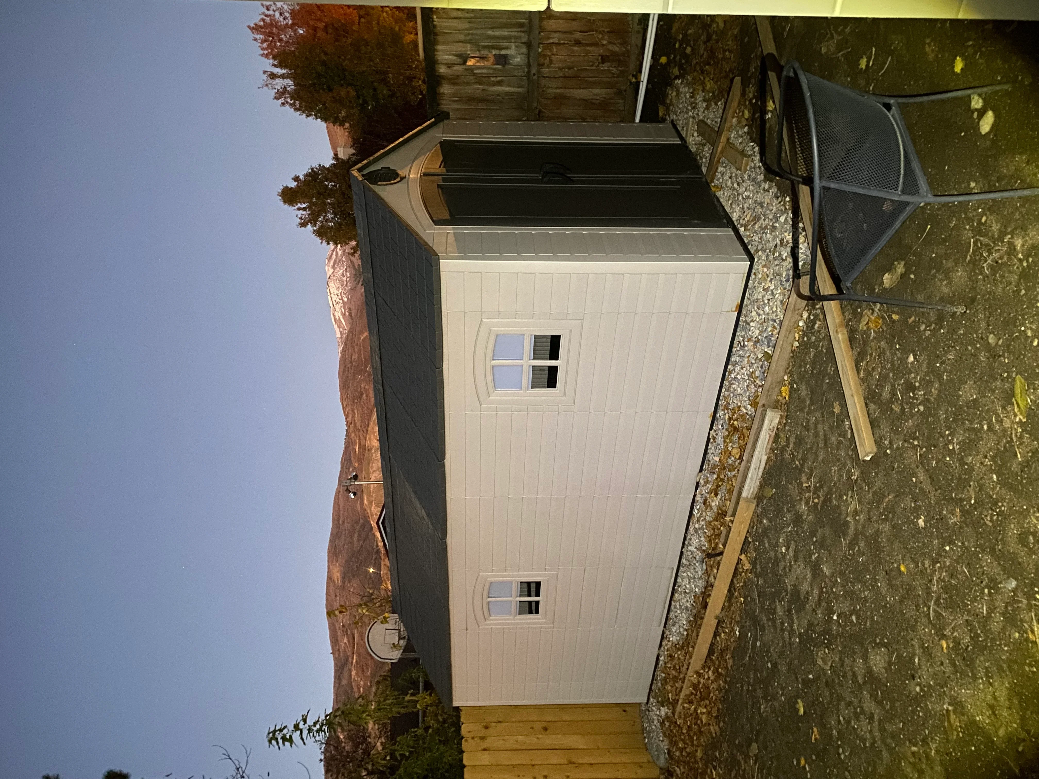 White vertical siding garden shed with gray metal roof and two window openings on wooden foundation
