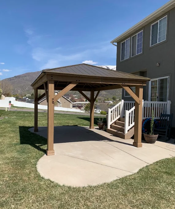 Wooden pergola with metal roof over concrete patio adjacent to home deck