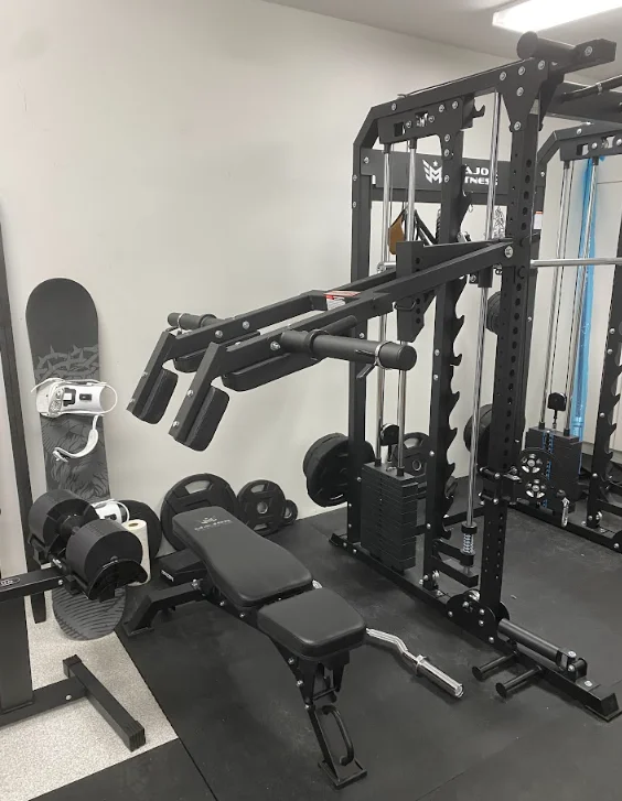 Black multi-station gym equipment with leg press and chest press, weight bench, and dumbbells installed in home fitness room
