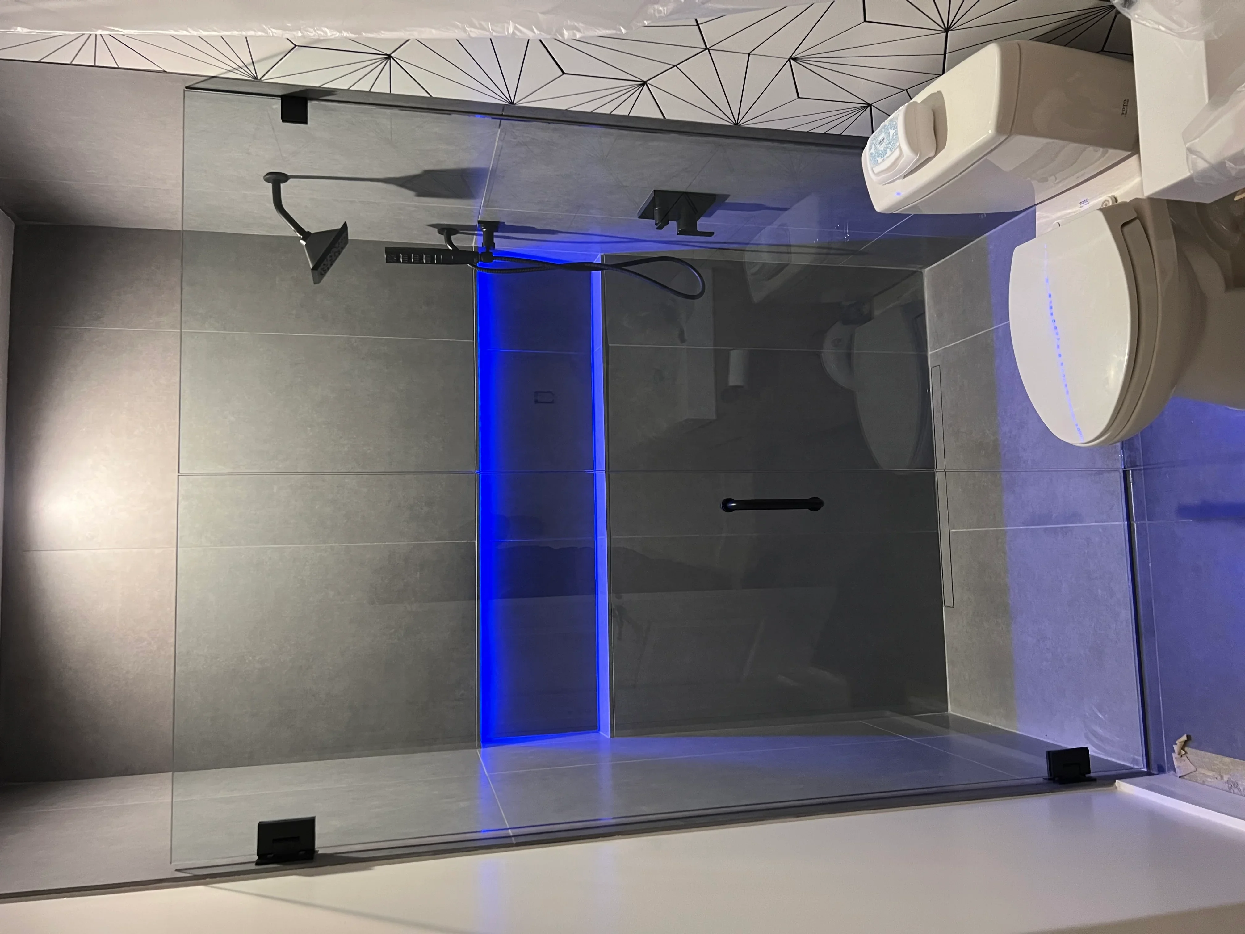 Frameless glass shower with gray tile walls, blue LED lighting, and black fixtures