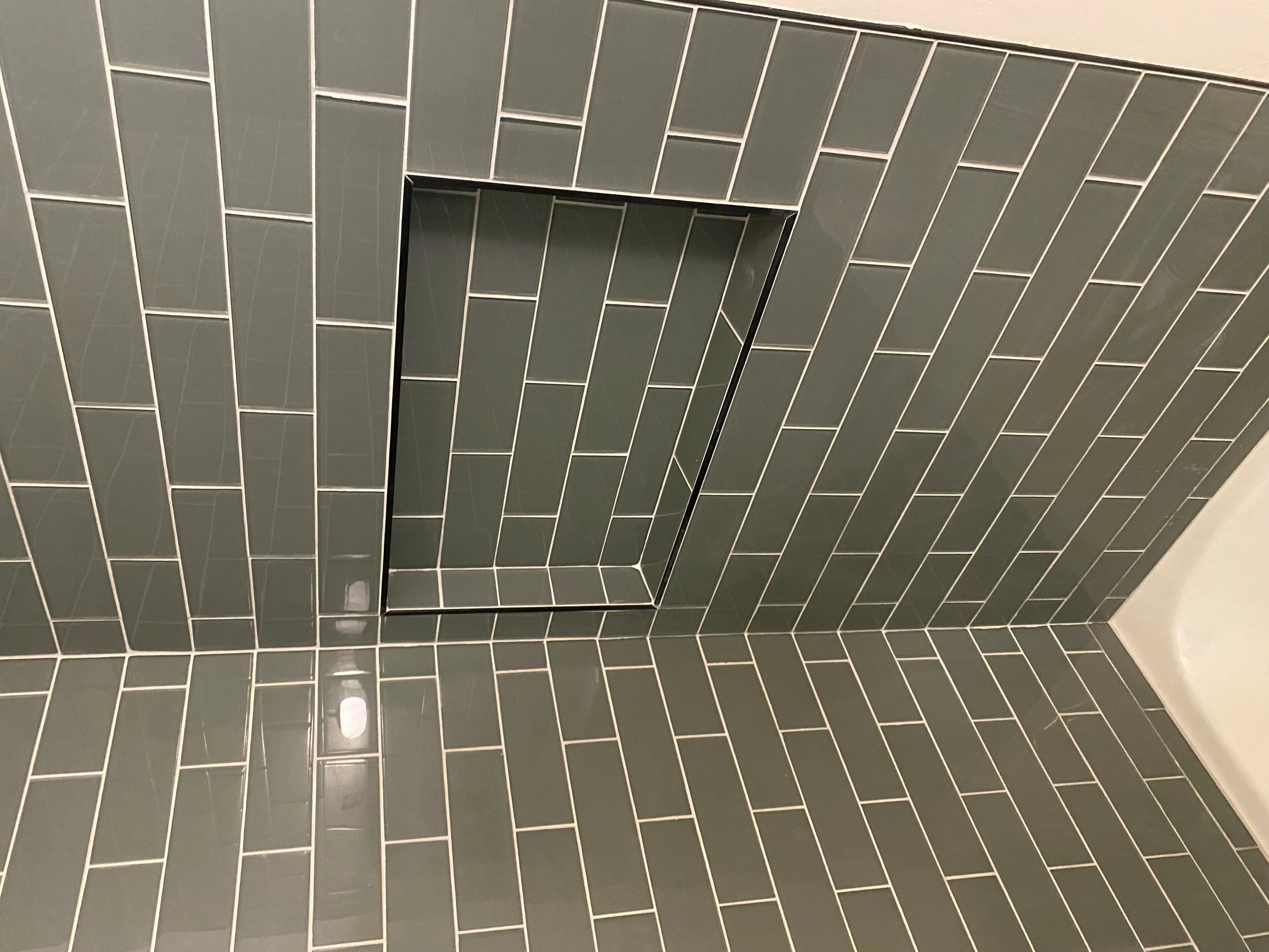 Gray herringbone pattern subway tiles with white grout lines in shower enclosure