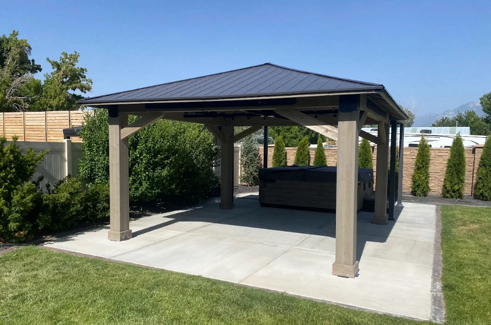 Concrete and wood gazebo with charcoal metal roof and beam framing on concrete pad