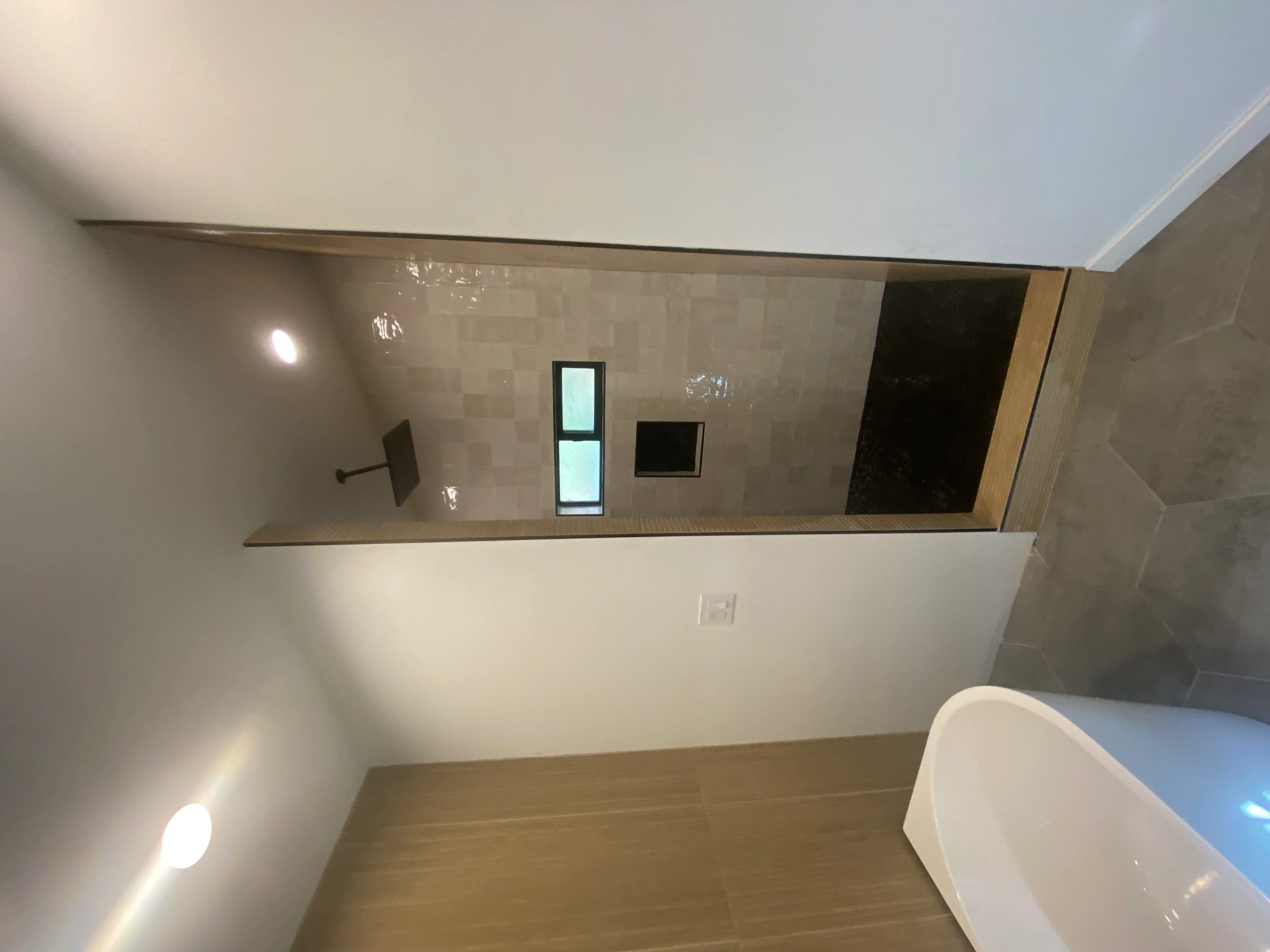 Bathroom with beige geometric tile walls, wood-trimmed niche shelving, recessed lighting, and freestanding tub